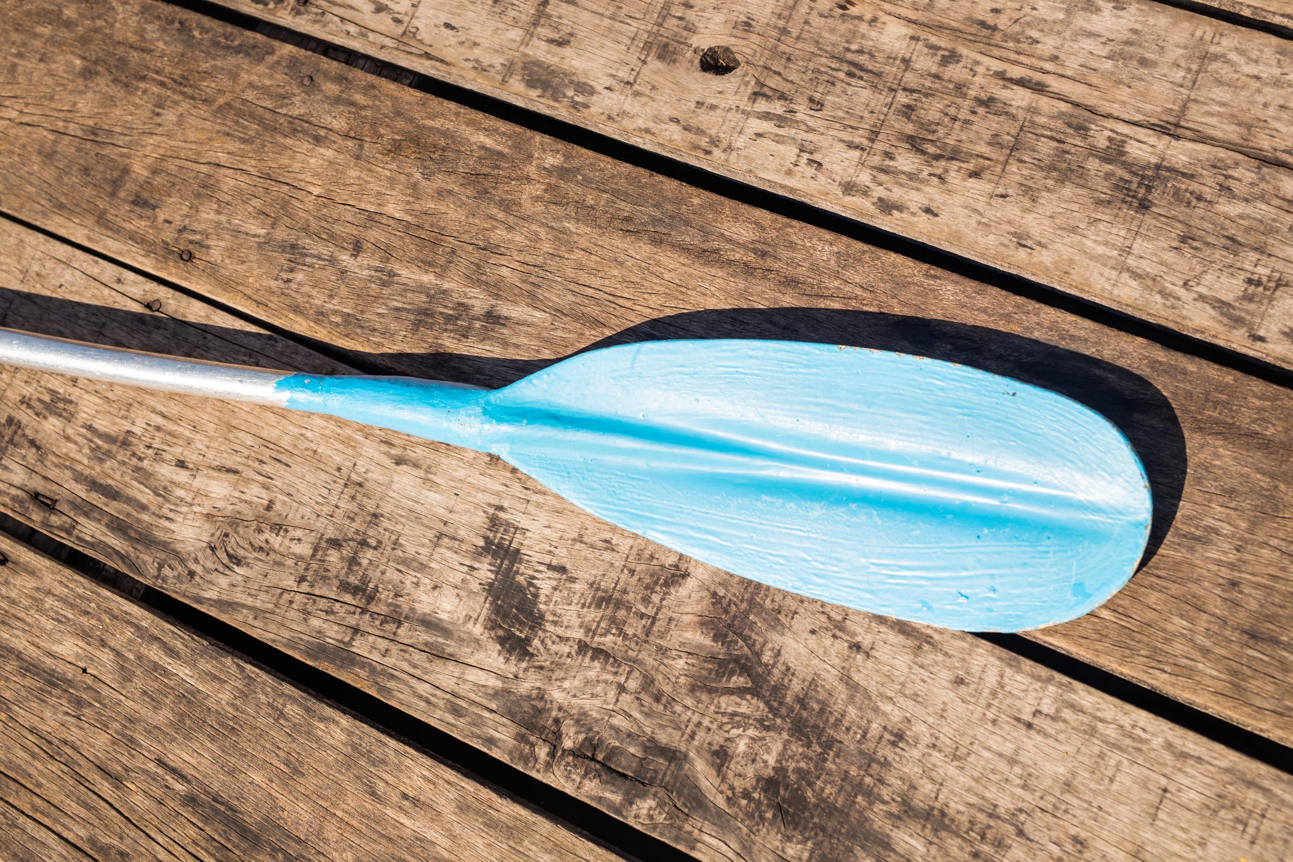 Blue plastic kayak paddle on wooden background pagay-scaled